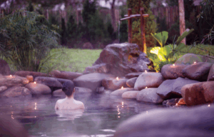 Person relaxing in outdoor sauna surrounded by stones.
